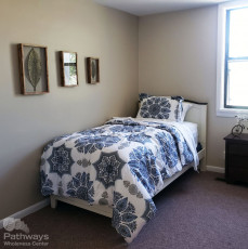 A small bedroom with a blue and white comforter in a drug rehab center.