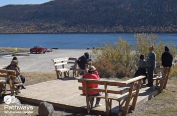A group of people undergoing drug addiction treatment sitting on benches near a lake.