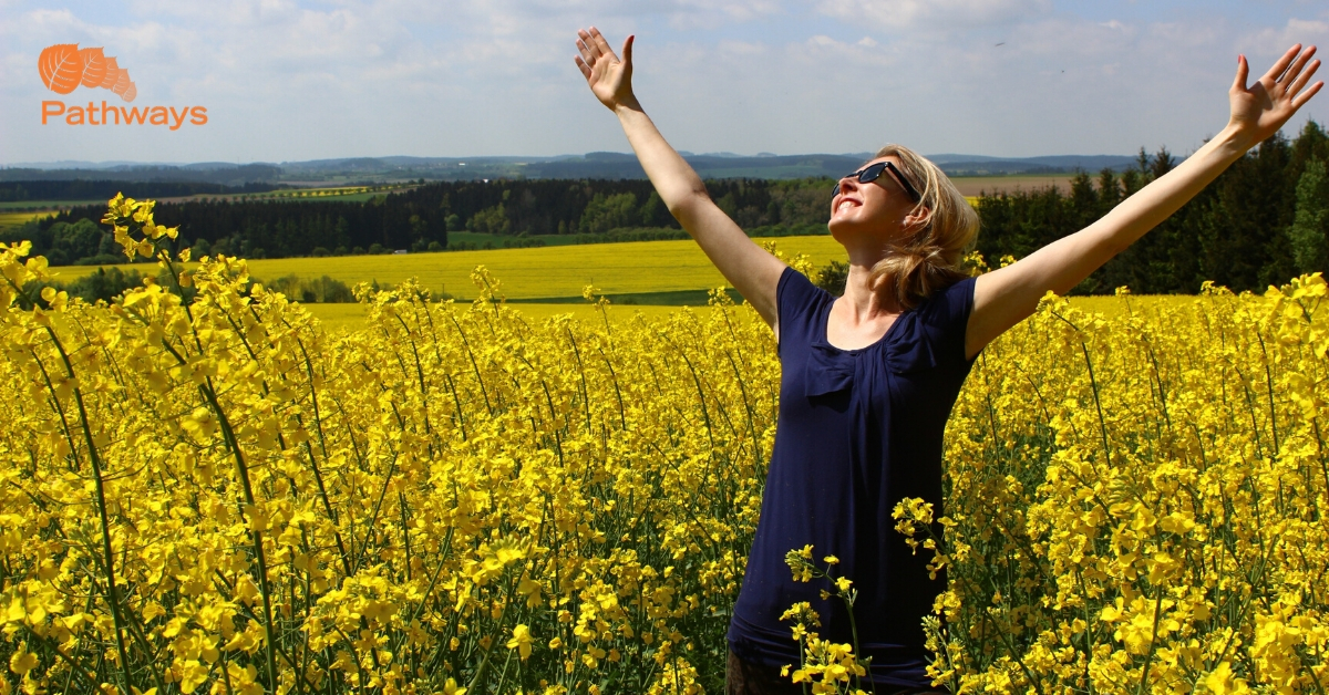 A woman in a yellow field with her arms outstretched, finding solace in drug rehab in Utah.