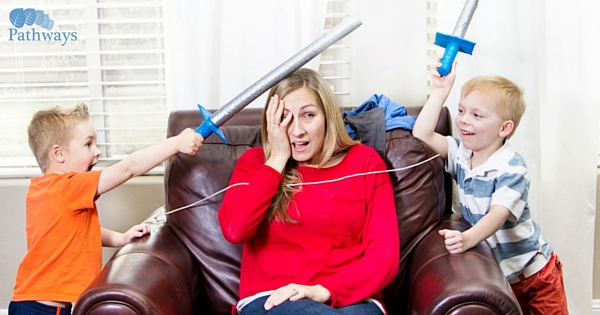 A woman and two children engaging in playful sword-fighting in a living room, exemplifying the importance of mental health care for families struggling with drug addiction.